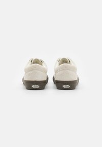 White suede sneakers with a textured finish and brown rubber soles. Features a logo on the heel and a rounded shape.