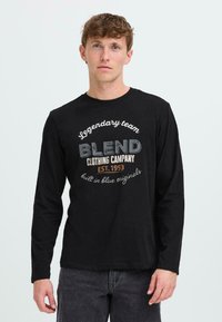 Juodas ilgomis rankovėmis marškinėliai su grafiniu spaudiniu, kuriame yra "Blend Clothing Company" ir "Legendary team" skirtingomis spalvomis.