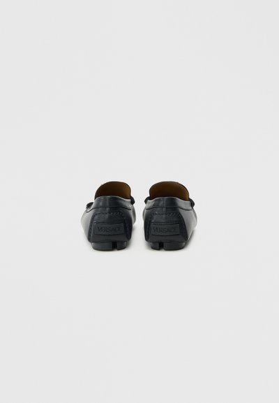 Czarne skórzane mokasyny z zaokrąglonym noskiem, wsuwane, z wytłoczonym logo z tyłu. Gładka faktura i minimalne przeszycia.