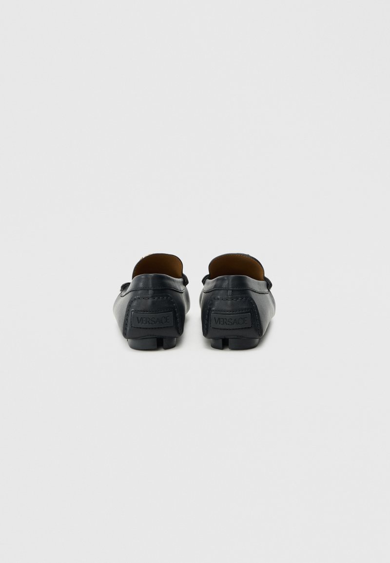 Schwarze Leder-Loafer mit abgerundetem Zehenbereich, Schlupfdesign und geprägt Logo auf der Rückseite. Glatte Textur und minimalistische Nähte.