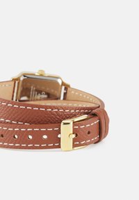 Bracelet de montre en cuir marron avec des surpiqûres blanches, quincaillerie dorée et boîtier carré. Cuir texturé et détail de boucle précis visibles.