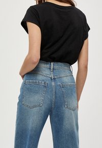 Černé tričko s vyhrnutými rukávy, doplněné světle modrými džíny s vysokým pasem, dvěma zadními kapsami a vybledlým efektem.