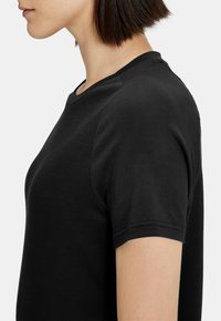 Camiseta corta negra de manga corta hecha de algodón suave. Presenta un cuello redondo y un sutil detalle de costura en las mangas y el hombro.