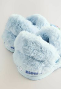 Pantofole di colore azzurro chiaro, realizzate in materiale morbido, con un esterno fluffy, forma rotonda e un dettaglio con il marchio sul lato.