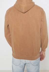 Brown hooded sweatshirt with a relaxed fit, soft texture, ribbed cuffs, and hem. Features a centered back seam and minimal detailing.