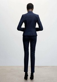 Marineblauwe getailleerde blazer met een aangesloten ontwerp, gecombineerd met slim-fit broeken. Heeft een gestructureerde stof en hoge hakken, gezien vanuit de achterkant.