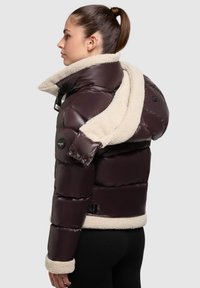 Giubbotto termico marrone con colletto in pelliccia crema a contrasto, design imbottito e accessori neri. Presenta una silhouette aderente.