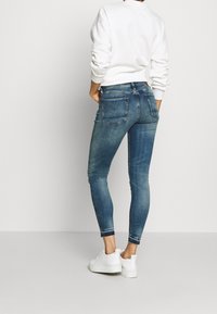 Tajta jeans i blekt blå denim med en figurnära passform. Har två bakfickor och diskret söm. Kombineras med en vit sweatshirt och sneakers.