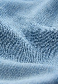 Ljust blå denimtyg med en strukturerad väv och mjuk yta, som visar ett subtilt diagonalt mönster som är typiskt för denimmaterial.