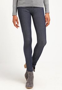 Vaqueros skinnies azul oscuro de mezclilla, con una textura suave y un ajuste ceñido, combinados con botines grises de tobillo con tacón de madera.