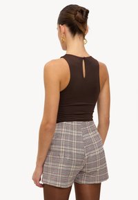 Débardeur marron ajusté avec un dos à trou clé, assorti à un short taille haute à motifs écossais dans des tons beige, noir et rouge.