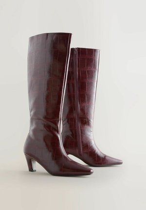 Burgundi színű, krokodil mintás bőrből készült, térd fölé érő csizmák, hegyes orral és közepes sarkúval. Oldalt cipzárral záródik.