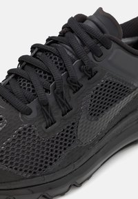 Svart sportskor med meshpaneler, tjocka sulor och runda snören. Märkbar kurvad design och Nike-logotyp på sidan.