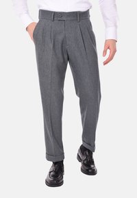 Pantaloni di lana grigi con una finitura testurizzata, caratterizzati da pieghe, una chiusura a un bottone e risvolti. Indossati con scarpe nere lucide.