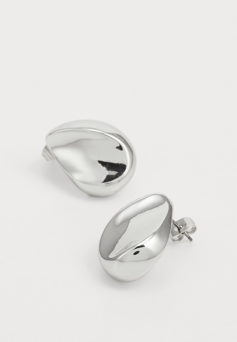 Boucles d'oreilles à clip en métal argenté, avec une surface lisse et polie et une forme ovale et courbée qui reflète la lumière. Pas d'éléments décoratifs supplémentaires.
