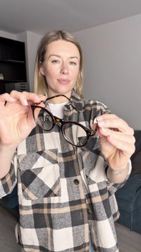 Okulary w kolorze tortoiseshell z okrągłymi oprawkami, przezroczystymi soczewkami i złotymi metalowymi akcentami na zawiasach. Noszący prezentuje okulary obiema dłoniami.