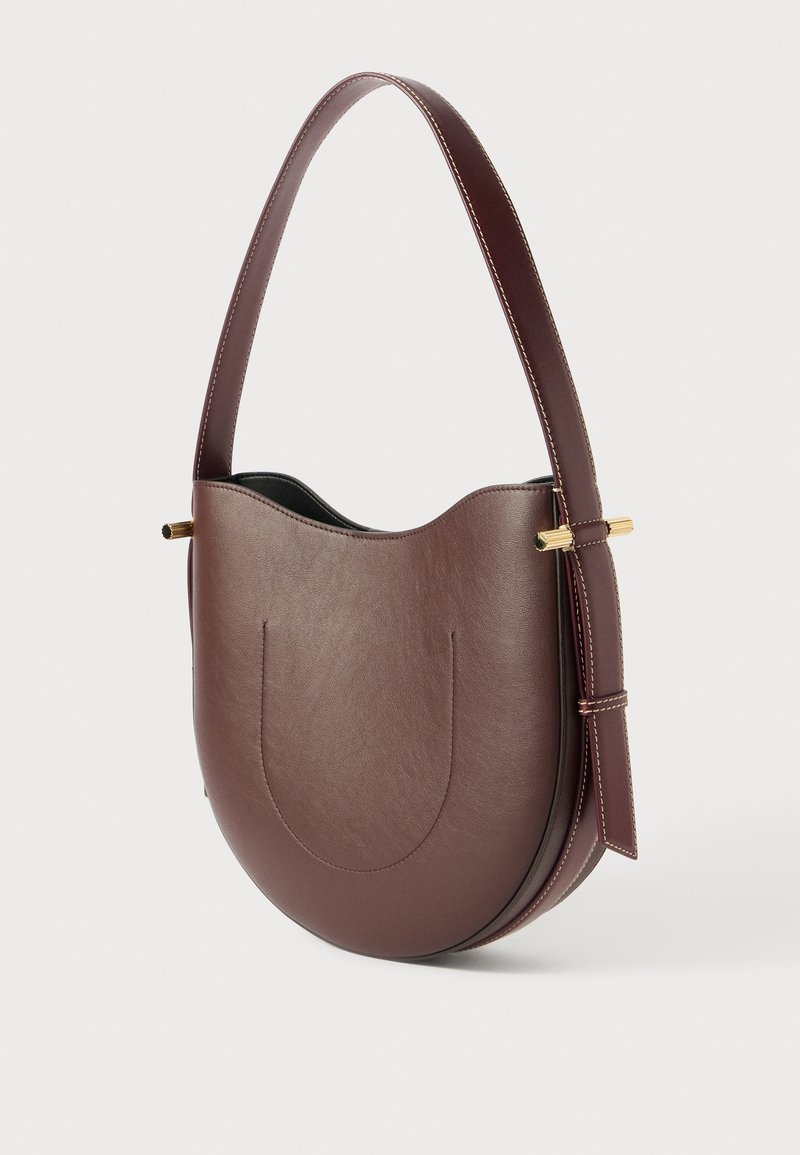 Bruine lederen handtas met een gebogen silhouet, een enkele schouderband en gouden accenten. Heeft een gladde textuur en een minimalistisch ontwerp.