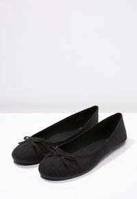 Chaussures en daim noir mat avec un bout rond et un accent en nœud sur le devant. L'intérieur est doublé, offrant une texture lisse. Convient pour un usage décontracté.