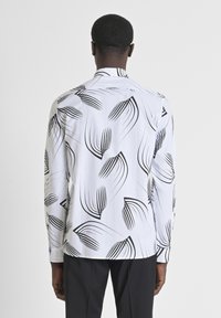 Camisa de manga larga de tela blanca con un patrón botánico negro, con un collar clásico y un dobladillo recto.