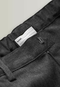 Schwarzer Stoffbund mit einem Label, auf dem "NAME" steht, und einem Reißverschluss. Die Textur wirkt glatt mit einem leicht glänzenden Finish.