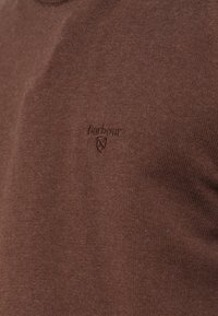 Barbour logó és pajzs embléma kis hímzéssel, egyező barna cérnával, barna kötött anyagon.