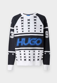 Svart og hvit strikket genser med v-hals, blå "HUGO" logo, og numeriske aksenter "3" og "9" med kryssmønster.