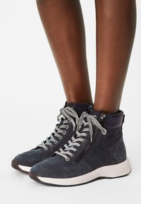 Höga sneakers i mörkblå mocka med vita och grå randiga snören, sidodragkedja och en lätt gummisula. Accentuerad häl i mörkare färg.