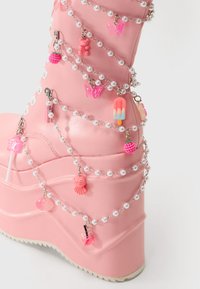 Botte à plateforme rose en matériau synthétique, ornée de chaînes en perles blanches et de charms variés, y compris des papillons et des glaces.