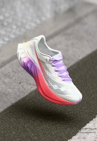 Scarpa da corsa con una parte superiore bianca e dettagli testurizzati, lacci viola e una suola con gradiente che passa dal rosa al bianco.