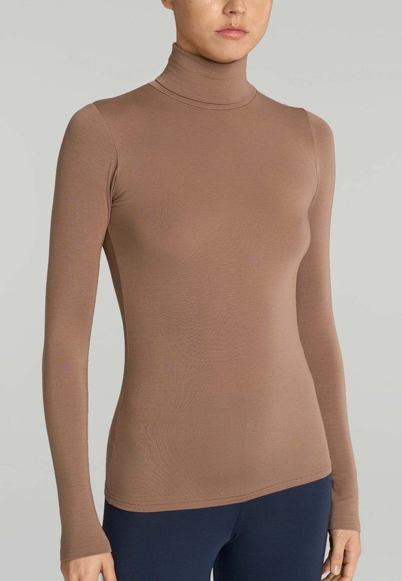 Maglia a maniche lunghe marrone a collo alto realizzata in tessuto morbido ed elasticizzato. Design aderente con collo alto e maniche senza cuciture, abbinata a pantaloni blu navy.