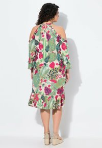 Vestido de estampado floral con mangas cortas, diseño de hombros descubiertos, base verde y dobladillo con volantes. Acentuado con patrones en rosa, rojo y negro.