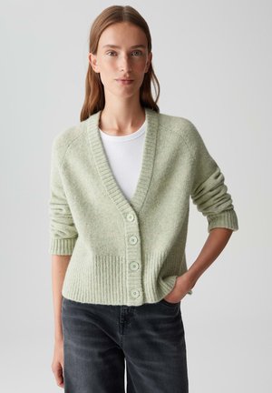 Cardigan vert clair avec ourlets et poignets côtes, présentant un col en V, cinq boutons et une texture douce, porté sur un haut blanc.