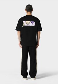 Juodas oversized T-shirt su grafiniu dizainu ant nugaros pastelinių spalvų. Poruojamas su juodomis kelnėmis, turinčiomis kreminės spalvos šonines juosteles.