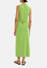 Zielona sukienka bez rękawów z dopasowaną górą, wycięciem na plecach i szeroką spódnicą. Zawiera detal z paskiem i guzikiem w talii. Teksturowany materiał.