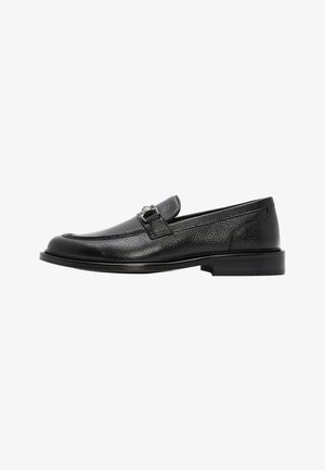 Mocasín para hombre de cuero negro con tacón bajo y detalle de hebilla metálica plateada en la parte superior.
