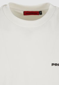 Weißes Baumwoll-T-Shirt mit rundem Halsausschnitt, schwarzem "VERBOTEN"-Text auf der Vorderseite und einem roten Etikett im Kragen. Größe S.
