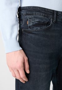 Σκούρο μπλε τζιν παντελόνι με ελαφρώς ξεθωριασμένο εφέ, πέντε τσέπες και μία μικρή πορτοκαλί ετικέτα μάρκας. Απαλή υφή υφάσματος και εφαρμογή που τονίζει το σώμα.