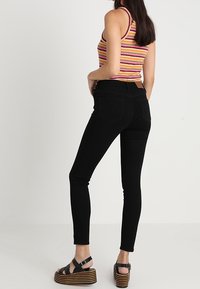 Svarta slim fit-jeans med hög midja, med en mjuk textur och en klassisk femfickorsstil. Kombineras med en flerfärgad randig linne och platåsandaler.