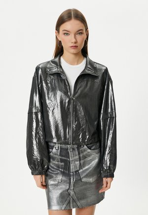 Metalen zwarte zip-up jack met een staande kraag, elastische manchetten en een cropped pasvorm, gecombineerd met een bijpassende zilveren spijkerrok.