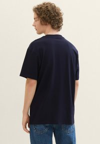 T-shirt navy a maniche corte con scollo rotondo classico, vestibilità morbida e materiale in cotone soffice, abbinato a jeans denim blu chiaro.