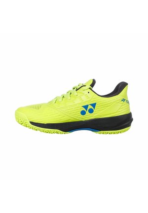 Scarpa sportiva giallo brillante con suola nera e logo blu, vista di profilo, con lacci e collarino imbottito alla caviglia.