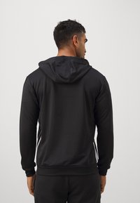 Schwarzer Hoodie mit weichem Textur, ausgestattet mit einer Fronttasche, verstellbarem Kordelzug und drei weißen Streifen entlang der Seiten.