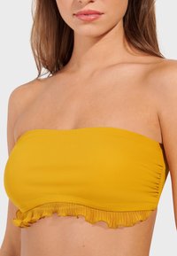 Yellow bandeau bikini top with ruffled trim. Smooth texture and stretchy material. Designed for a close fit, ideal for swimwear.