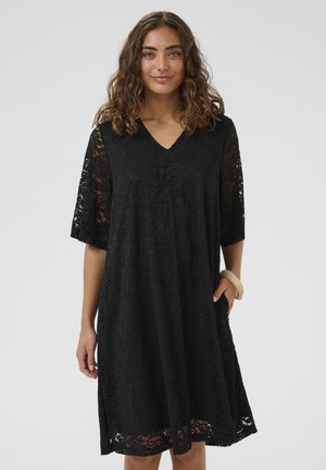 Fekete csipkeruha rövid, bővülő ujjal és V-nyakkivágással. Finom virágmintákkal díszített, kényelmes szabású, oldalzsebekkel.