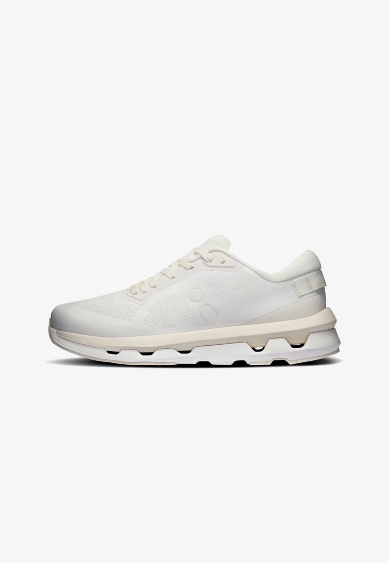 Basket de sport blanche basse avec tige en mesh texturé, semelle intermédiaire beige, détails uniques de découpes dans la semelle et fermeture à lacets, vue latérale.