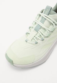 Hellgrüner Sportschuh mit strukturiertem Obermaterial, weißen Schnürsenkeln und dezentem Branding. Verfügt über eine geformte Zehenkappe und eine geriffelte weiße Sohle.
