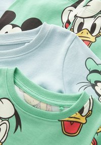 Drie t-shirts: één lichtblauw, twee groene met prints van cartoonfiguren. Geribbelde halslijnen in contrasterende kleuren. Zacht katoenen materiaal.