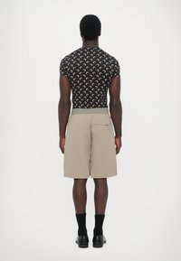 Svart kortärmad skjorta med ett beige halvmånemönster, tillsammans med beige shorts med sidoficka och elastiskt midjeband.