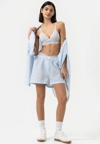 Lichtblauw gestreepte shirt, witte kanten bralette en bijpassende shorts. Zachte stof, ontspannen pasvorm, kantafwerking op het shirt en de shorts. Witte sneakers.