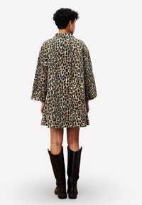 Oversized jas met luipaardprint, een kraag, lange mouwen en een uitlopende zoom, gecombineerd met zwarte leren laarzen tot de knie.